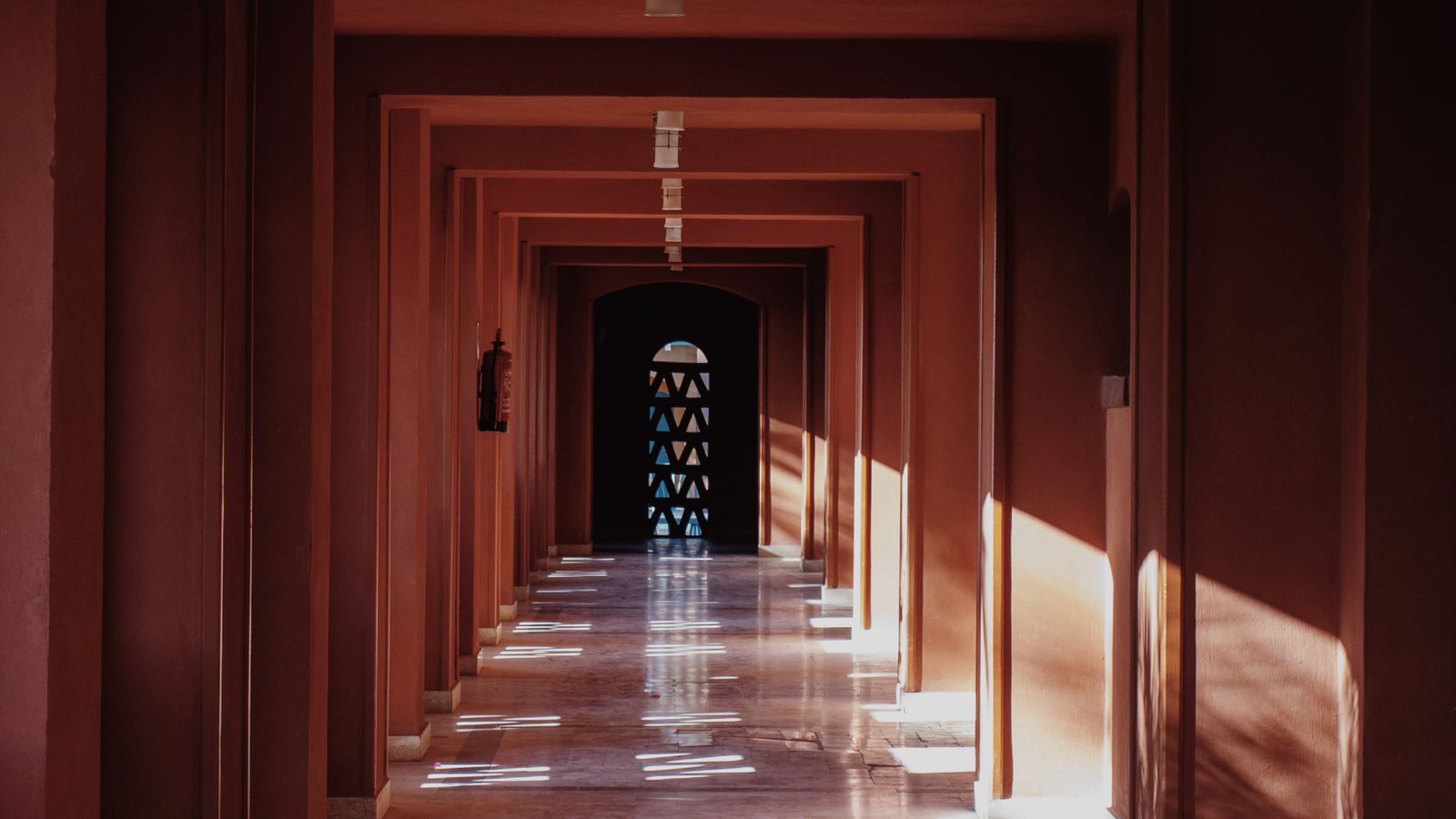 Sunlight falling in bright patches down a long terracotta colonnade